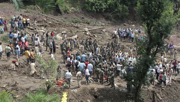 People watch army soldiers and rescue workers recover bodies of landslide victims even as they try to pull out two buses that were covered in mud after a landslide triggered by heavy monsoon rain in Urla village, Himachal Pradesh state, India - Sputnik Afrique
