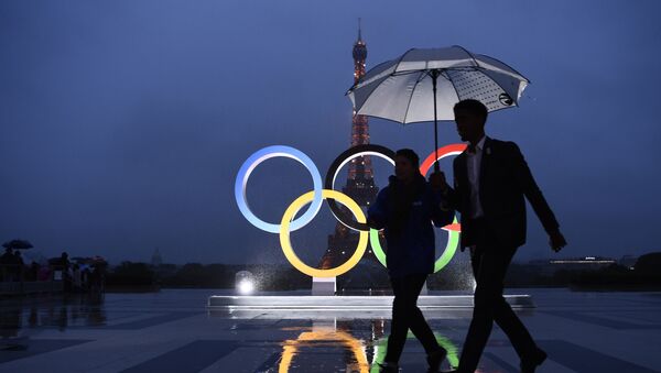 People carrying an umbrella walk past the Olympics Rings on the Trocadero Esplanade near the Eiffel Tower in Paris, on September 13, 2017, after the International Olympic Committee named Paris host city of the 2024 Summer Olympic Games. - Sputnik Afrique