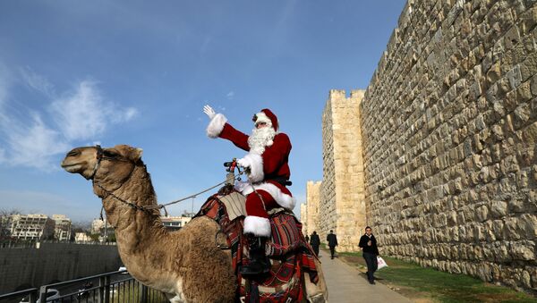 Israeli-Arab Issa Kassissieh rides a camel wearing a Santa Claus costume during the annual Christmas tree distribution by the Jerusalem municipality in Jerusalem's Old City - Sputnik Afrique