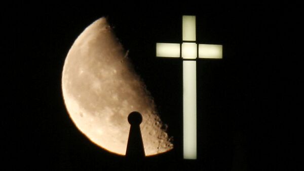 A third quarter Buck Moon rises behind a spire on the top of the bell tower next to a lighted cross - Sputnik Afrique
