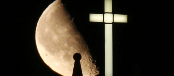 A third quarter Buck Moon rises behind a spire on the top of the bell tower next to a lighted cross - Sputnik Afrique