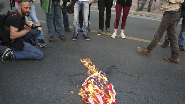 Des manifestants avaient brûlé un drapeau américain à l'extérieur de l'ambassade des États-Unis à Athènes, le vendredi 13 avril 2018, lors d'un rassemblement contre une éventuelle intervention militaire occidentale en Syrie - Sputnik Afrique