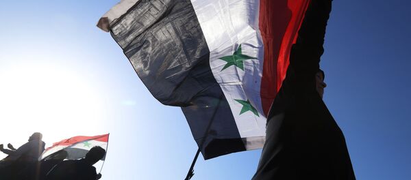 A Syrian government supporter holds up a Syrian national flag as he chants slogans against U.S. President Trump during demonstrations following a wave of U.S., British and French military strikes to punish President Bashar Assad for suspected chemical attack against civilians, in Damascus, Syria, Saturday, April 14, 2018 - Sputnik Afrique