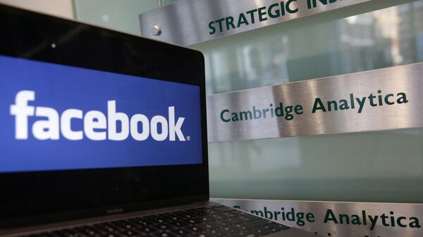 A laptop showing the Facebook logo is held alongside a Cambridge Analytica sign at the entrance to the building housing the offices of Cambridge Analytica, in central London on March 21, 2018 - Sputnik Afrique
