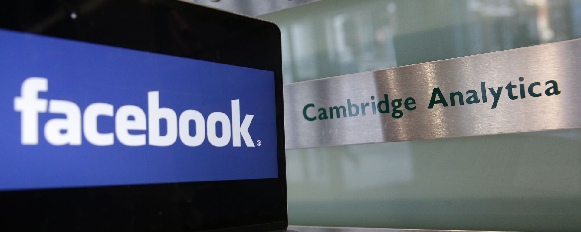 A laptop showing the Facebook logo is held alongside a Cambridge Analytica sign at the entrance to the building housing the offices of Cambridge Analytica, in central London on March 21, 2018 - Sputnik Afrique, 1920, 16.05.2018