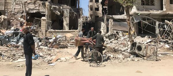 People stand in front of damaged buildings, in the town of Douma, the site of a suspected chemical weapons attack, near Damascus, Syria, Monday, April 16, 2018 People stand in front of damaged buildings, in the town of Douma, the site of a suspected chemical weapons attack, near Damascus, Syria, Monday, April 16, 2018 - Sputnik Afrique