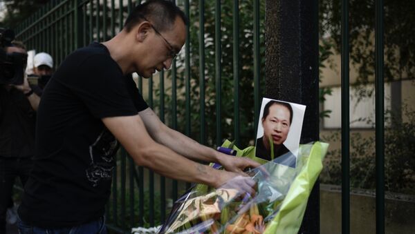 A member of the Chinese commmunity arranges a display of flowers besides a photograph of slain Chinese tailor Zhang Chaolin during a candlelight vigil in Aubervilliers on August 7, 2017, on the first anniversary of the fatal mugging of the Chinese tailor. Chinese tailor Zhang Chaolin, aged 49, was assaulted by three men in the streets in Aubervilliers on August 7, 2016 and died 5 days later from a coma. - Sputnik Afrique