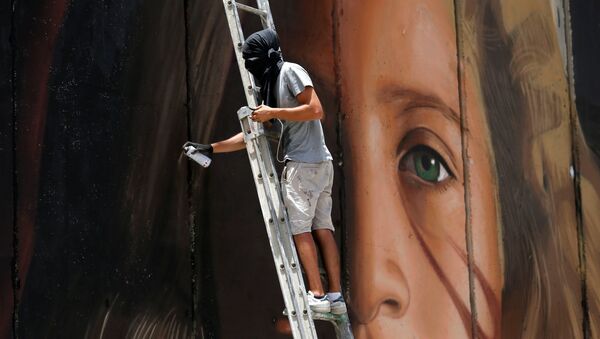 A foreign artist paints on the Israeli wall a mural depicting Palestinian teen Ahed Tamimi who is detained by Israel, in Bethlehem, in the occupied West Bank, July 25, 2018. - Sputnik Afrique