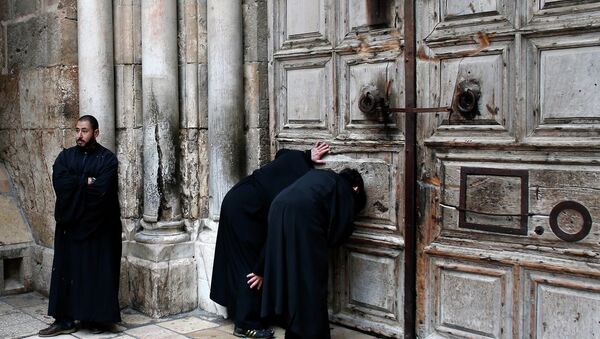 Christian Orthodox priests look through a hole in the main door of the Church of the Holy Sepulchre, before the Holy fire ceremony around Jesus' tomb, in Jerusalem’s Old City - Sputnik Afrique