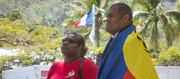 A man, right, drapes the flag of New Caledonia on his shoulders as the French flag flies in the background as he and a woman line up to cast their votes at a polling station in Noumea, New Caledonia, as part of an independence referendum, Sunday, Nov. 4, 2018. - Sputnik Afrique