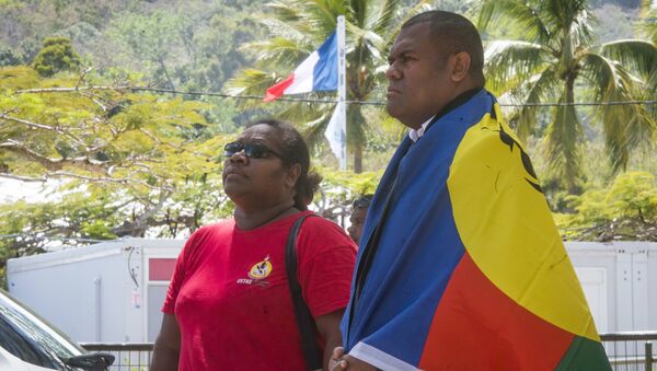 A man, right, drapes the flag of New Caledonia on his shoulders as the French flag flies in the background as he and a woman line up to cast their votes at a polling station in Noumea, New Caledonia, as part of an independence referendum, Sunday, Nov. 4, 2018. - Sputnik Afrique