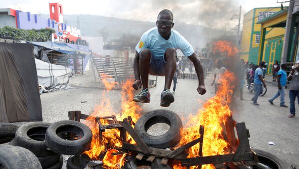 Протестующий перепрыгивает через горящую баррикаду во время акции протеста против правительства на улицах Порт-о-Пренса, Гаити - Sputnik Afrique