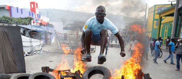 Протестующий перепрыгивает через горящую баррикаду во время акции протеста против правительства на улицах Порт-о-Пренса, Гаити - Sputnik Afrique