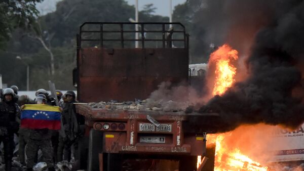 Venezuelan security forces display a national flag next to a truck which was burnt during the weekend when trying to enter the country with humanitarian aid, during clashes with supporters of Venezuelan opposition leader Juan Guaido on the Venezuelan side of the Francisco de Paula Santander International Bridge, as seen from Cucuta, Colombia, on February 25, 2019. - Sputnik Afrique