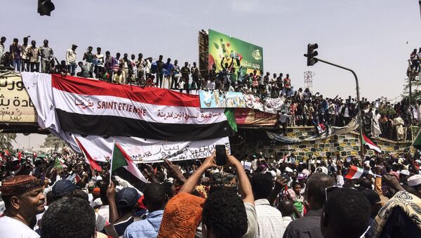 Demonstrators gather in Sudan's capital of Khartoum, Friday, April 12, 2019. The Sudanese protest movement has rejected the military's declaration that it has no ambitions to hold the reins of power for long after ousting the president of 30 years, Omar al-Bashir. The writing on the Sudanese flag says 'With the participation of the Sudanese in Saint Etienne, France.' - Sputnik Afrique