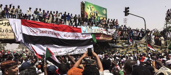 Demonstrators gather in Sudan's capital of Khartoum, Friday, April 12, 2019. The Sudanese protest movement has rejected the military's declaration that it has no ambitions to hold the reins of power for long after ousting the president of 30 years, Omar al-Bashir. The writing on the Sudanese flag says 'With the participation of the Sudanese in Saint Etienne, France.' - Sputnik Afrique
