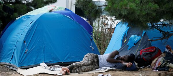 A migrant sleeps next to tents installed in a street near the entrance of the reception center for migrants and refugees at porte de La Chapelle, north of Paris, France, July 6, 2017 - Sputnik Afrique