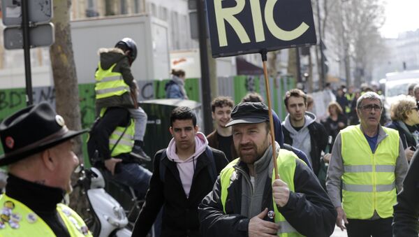 A Yellow Vest protester holds a sign reading RIC (Citizens Initiated Referendum), during an anti-government demonstration called by the 'Yellow Vest' (gilets jaunes) movement in Paris, on March 23, 2019. Demonstrators hit French city streets again on March 23, for a 19th consecutive week of nationwide protest against the French President's policies and his top-down style of governing, high cost of living, government tax reforms and for more social and economic justice. - Sputnik Afrique