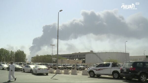 In this image made from a video broadcast on the Saudi-owned Al-Arabiya satellite news channel on Saturday, Sept. 14, 2019, a man walks through a parking lot as the smoke from a fire at the Abqaiq oil processing facility can be seen behind him in Buqyaq, Saudi Arabia. Drones launched by Yemen's Houthi rebels attacked the world's largest oil processing facility in Saudi Arabia and another major oilfield Saturday, sparking huge fires at a vulnerable chokepoint for global energy supplies - Sputnik Afrique
