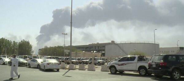 In this image made from a video broadcast on the Saudi-owned Al-Arabiya satellite news channel on Saturday, Sept. 14, 2019, a man walks through a parking lot as the smoke from a fire at the Abqaiq oil processing facility can be seen behind him in Buqyaq, Saudi Arabia. Drones launched by Yemen's Houthi rebels attacked the world's largest oil processing facility in Saudi Arabia and another major oilfield Saturday, sparking huge fires at a vulnerable chokepoint for global energy supplies - Sputnik Afrique