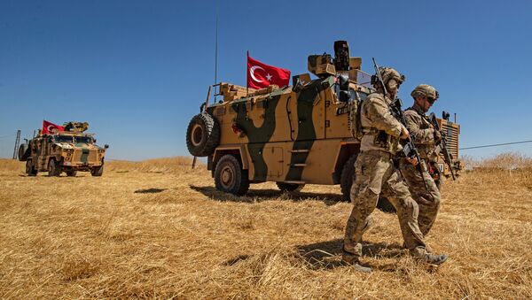 (FILES) In this file photo taken on September 08, 2019 US troops walk past a Turkish military vehicle during a joint patrol with Turkish troops in the Syrian village of al-Hashisha on the outskirts of Tal Abyad town along the border with Turkish troops - Sputnik Afrique
