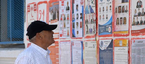 Un Tunisien devant les affiches des différents candidats aux législatives tunisiennes Un Tunisien devant les affiches des différents candidats aux législatives tunisiennes - Sputnik Afrique