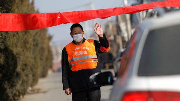 A village committee member wearing face mask and vest, stops a car for checking as he guards at the entrance of a community to prevent outsiders from entering - Sputnik Afrique