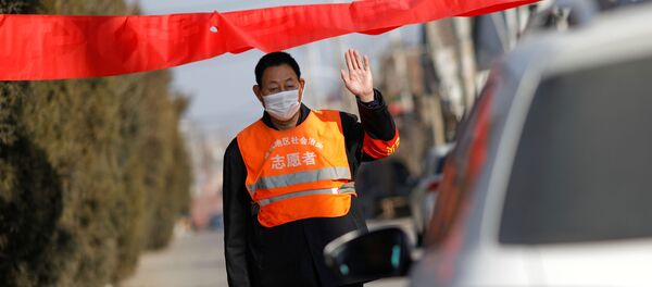 A village committee member wearing face mask and vest, stops a car for checking as he guards at the entrance of a community to prevent outsiders from entering - Sputnik Afrique