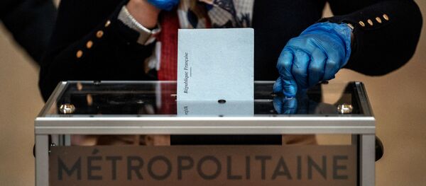 An election official wearing plastic gloves attends the ballot box in a polling station of Lyon on March 15, 2020 during the first round of the mayoral elections. Officials have been told to disinfect voting booths and ballot boxes throughout the day, and sinks and hand gels will be made available. People will be urged to get in and out quickly to avoid lines, and floor markings will be laid out to ensure they stay one metre (3.3 feet) from one another. Authorities have already eased proxy voting rules for people at risk or infected with coronavirus and ordered to confine themselves to their homes, as well as for people in retirement homes. People can also come with their own pens for marking ballots. JEFF PACHOUD / AFP - Sputnik Afrique