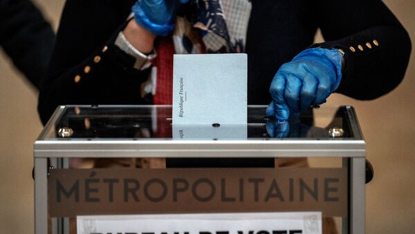 An election official wearing plastic gloves attends the ballot box in a polling station of Lyon on March 15, 2020 during the first round of the mayoral elections. Officials have been told to disinfect voting booths and ballot boxes throughout the day, and sinks and hand gels will be made available. People will be urged to get in and out quickly to avoid lines, and floor markings will be laid out to ensure they stay one metre (3.3 feet) from one another. Authorities have already eased proxy voting rules for people at risk or infected with coronavirus and ordered to confine themselves to their homes, as well as for people in retirement homes. People can also come with their own pens for marking ballots. JEFF PACHOUD / AFP - Sputnik Afrique