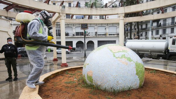 Un travailleur vêtu d'une combinaison de protection désinfecte une sculpture en forme de globe, à la suite de l'épidémie de coronavirus (COVID-19), à Alger, en Algérie, le 23 mars 2020. - Sputnik Afrique