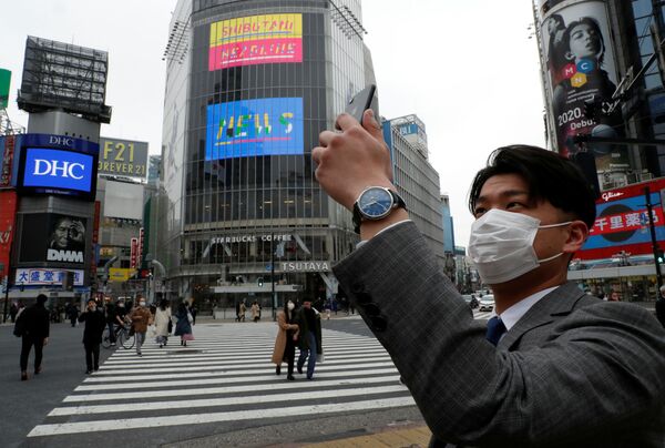 Un homme portant un masque de protection prend en photo, à midi, un croisement dans l'arrondissement de Shibuya à Tokyo pendant la pandémie de coronavirus - Sputnik Afrique